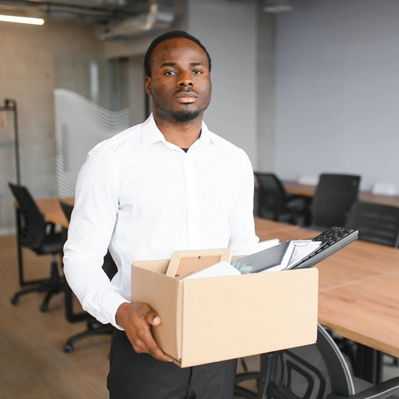 Retrenched employee who has been retrenched carrying a box of his things in an office setting.