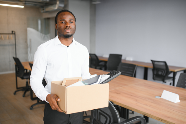 Retrenched employee who has been retrenched carrying a box of his things in an office setting.