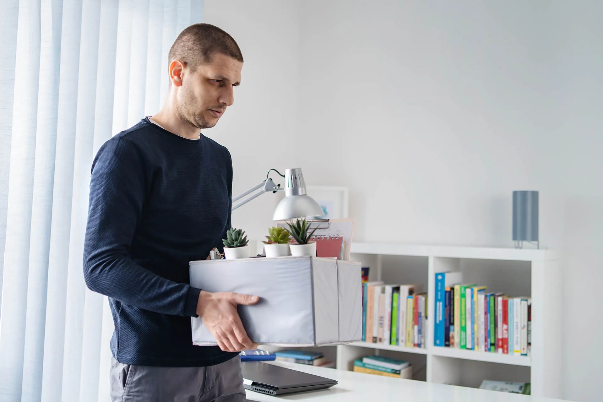 Man who has been retrenched carrying a box of his things from his office